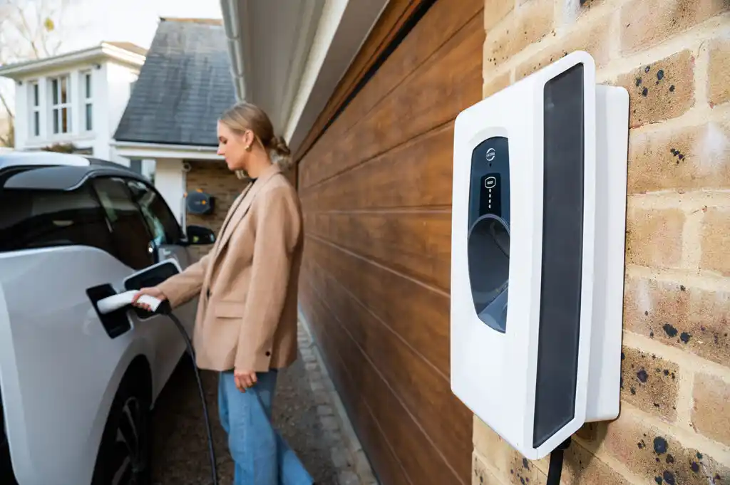 •	Woman plugging an electric vehicle into a home charging point - residential EV charger installation